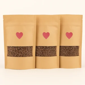 Three kraft paper pouches of ceremonial-grade cacao with heart labels, filled with chopped cacao pieces, displayed against a white background.