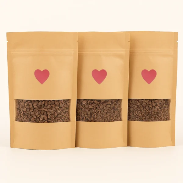 Three kraft paper pouches of ceremonial-grade cacao with heart labels, filled with chopped cacao pieces, displayed against a white background.